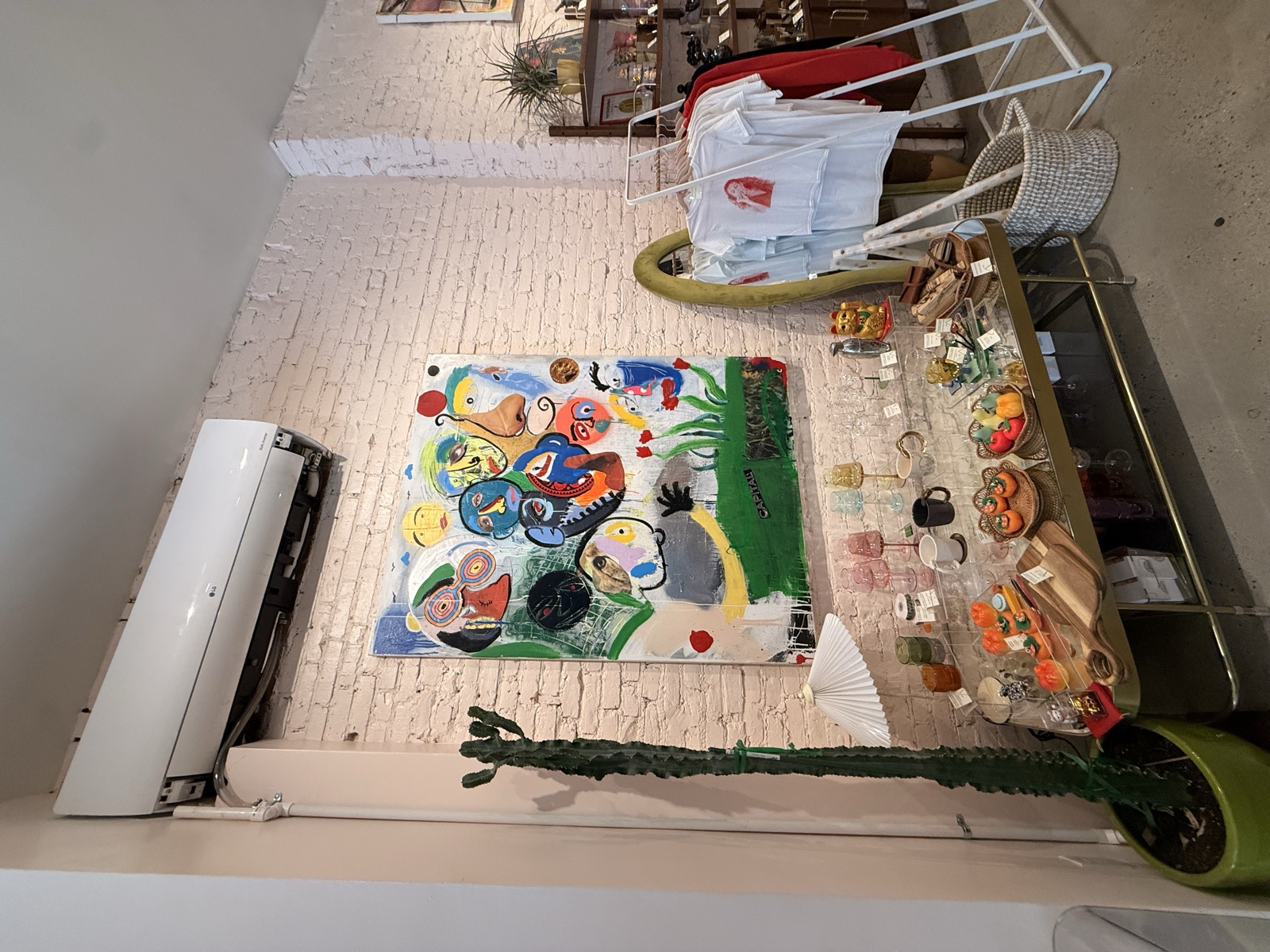 Large abstract face painting on white brick wall, with handcrafted display table and branded apparel rack at Mighty Lucky