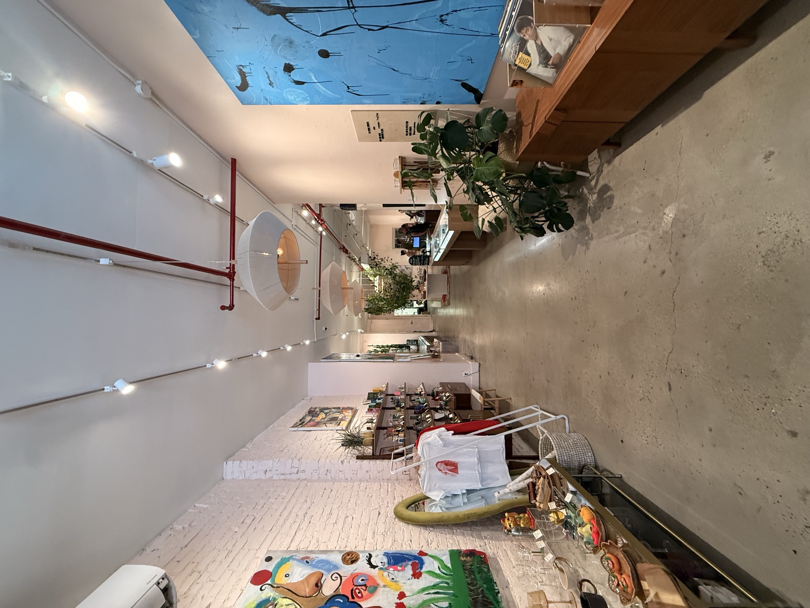 Long gallery view of Mighty Lucky — white brick walls, polished concrete, abstract paintings, plants throughout