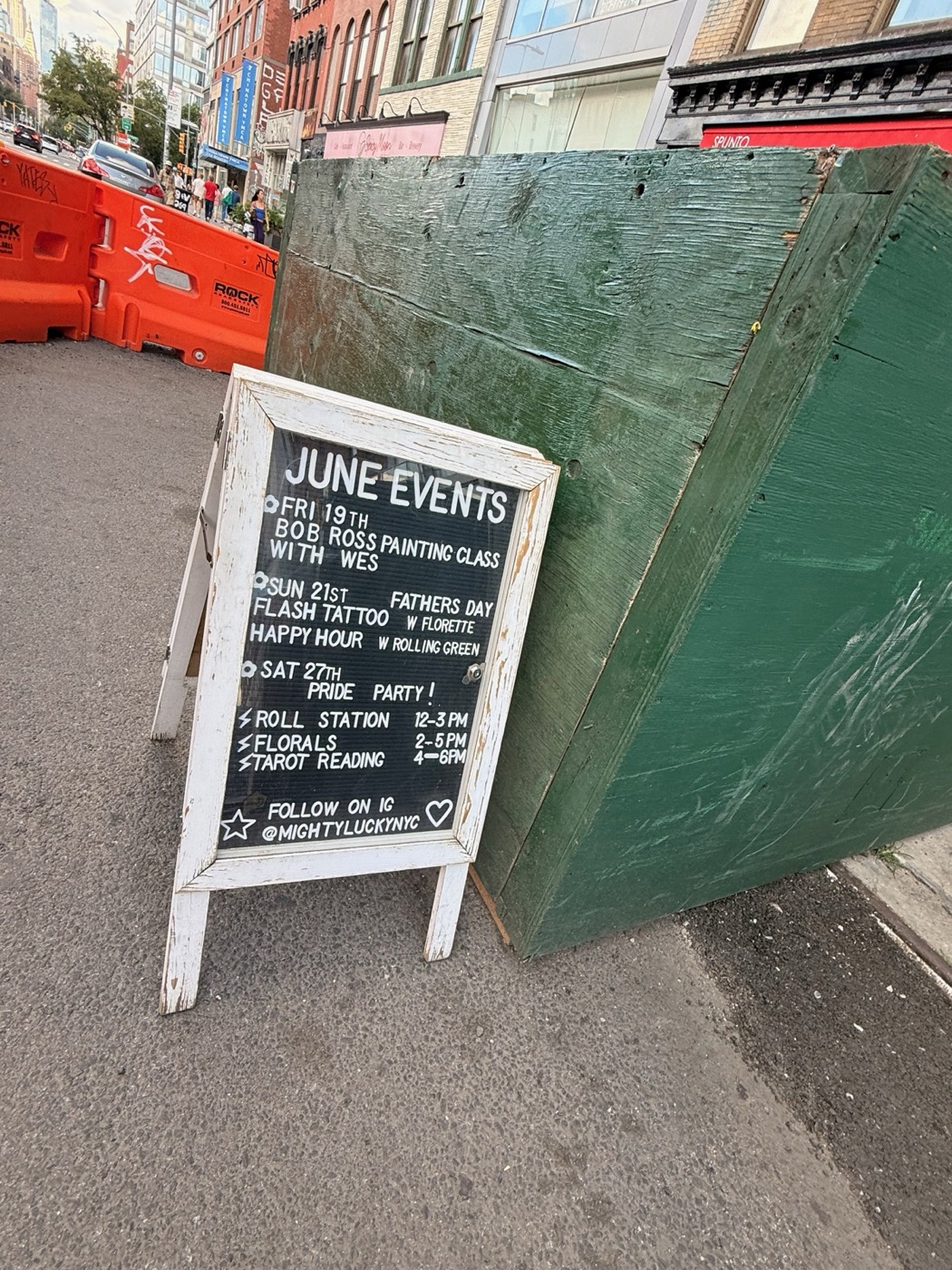 Mighty Lucky sidewalk chalkboard listing June events: Bob Ross painting class, Father's Day flash tattoo, happy hour, and a Pride party with roll station, florals and tarot reading